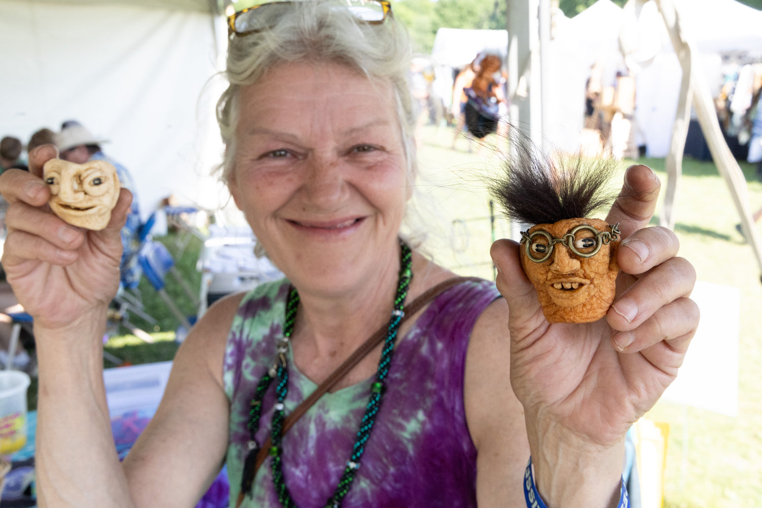 Woman holding two small figurines with faces at an outdoor event