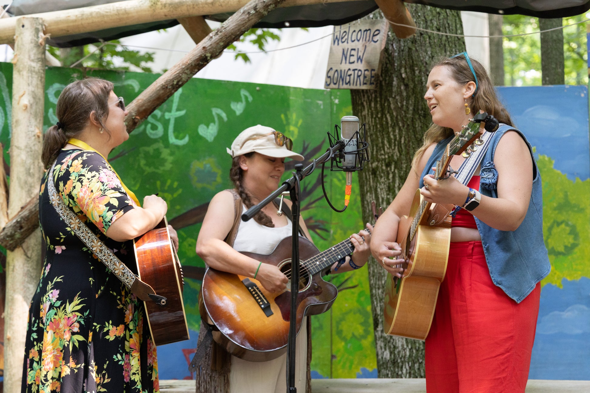 Three women playing guitars outdoors with a colorful backdrop
