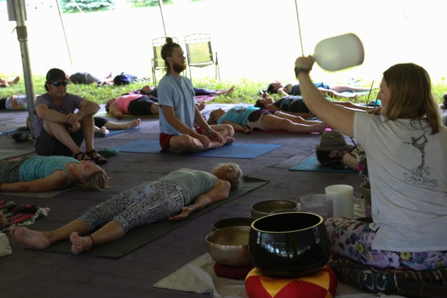 Group yoga session with a person holding a bell in an outdoor setting