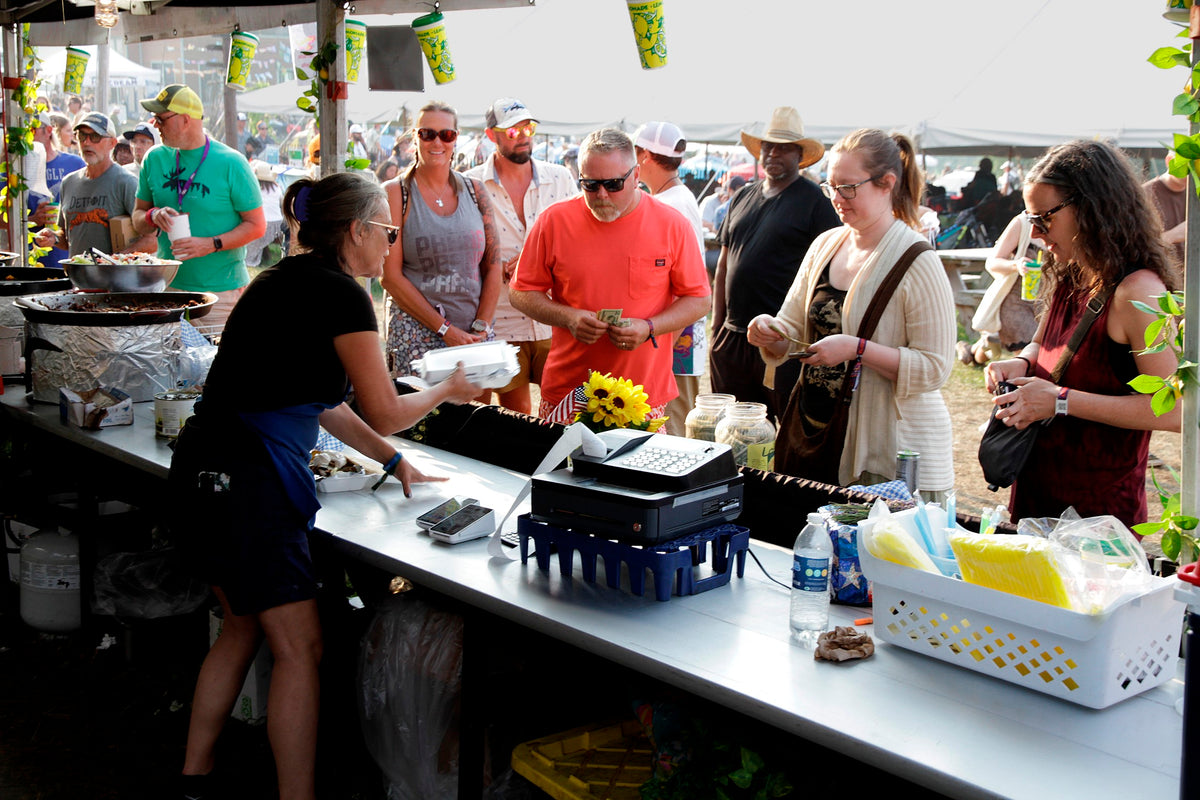 People shopping at an outdoor farmers market with a vendor and customers.