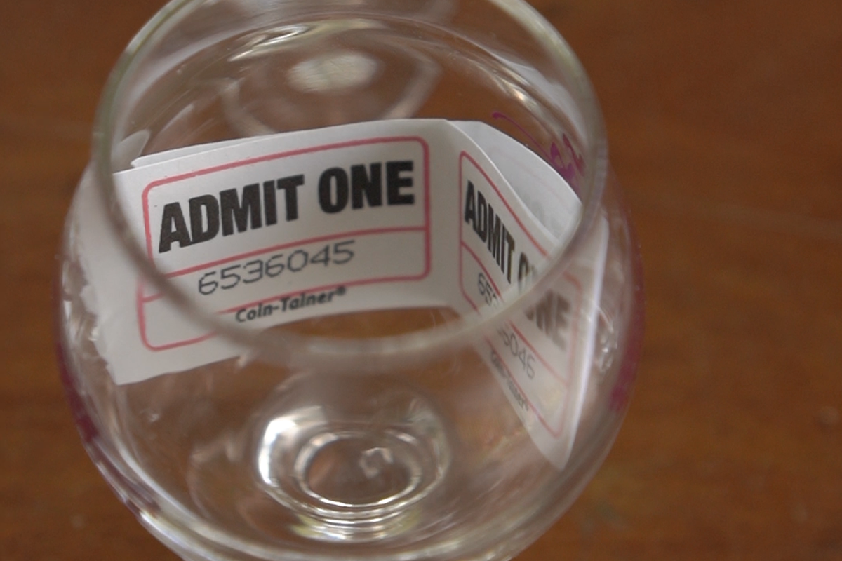 Clear glass with 'Admit One' ticket attached on a wooden surface