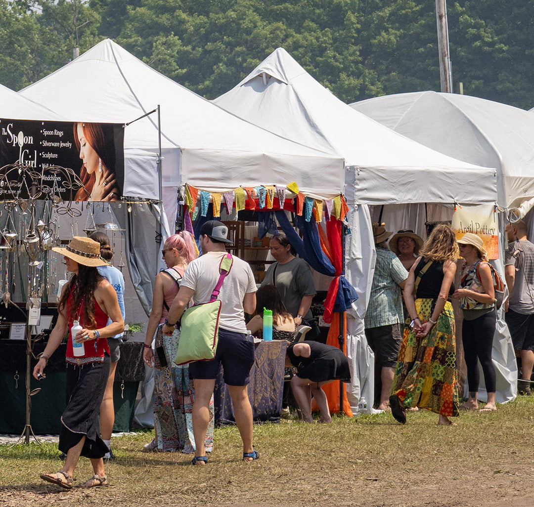 People at a festival under white tents with colorful decorations.